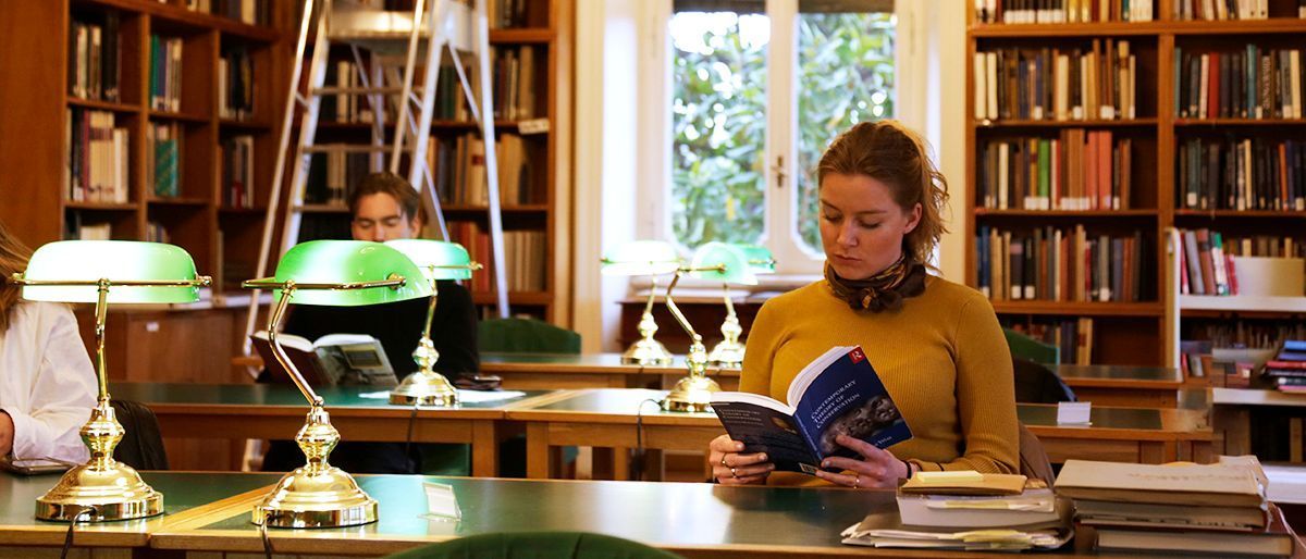 Tre personer sitter og leser bøker i et bibliotek.
