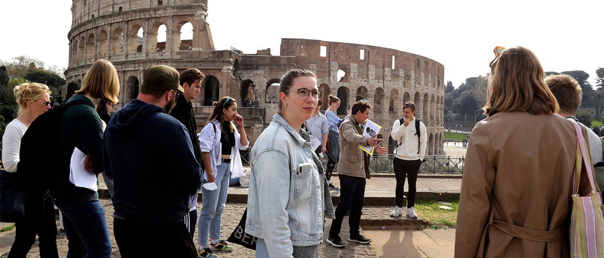 Cirka 15 mennesker står ved Colosseum i Roma. 
