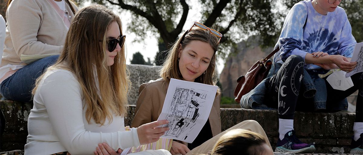 To kvinnelige studenter sitter ute på i en trapp og kikker på et ark. 