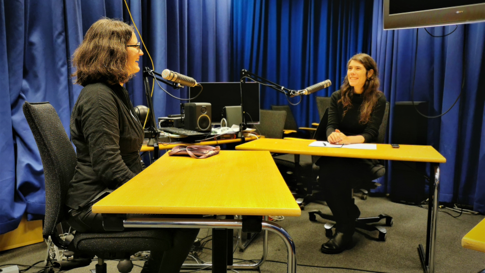 Two women talking to each other and recording a podcast.