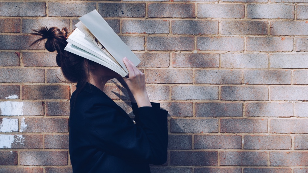 Woman holding a book up against her face. Photo.