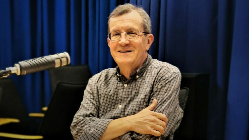 Man sitting at a desk with a microphone, smiling. 