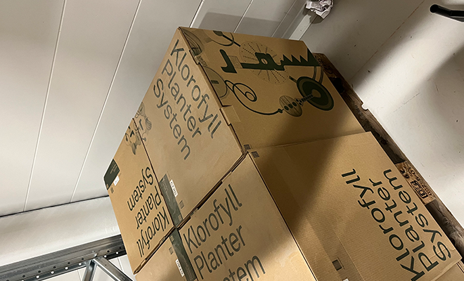 Cardboard boxes are piled on top of each other. Words such as "chloropfyll" and "plants" are written all over the boxes. 