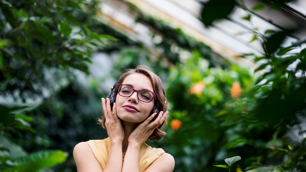 A woman is listening to music on her earphones in a greenhouse.