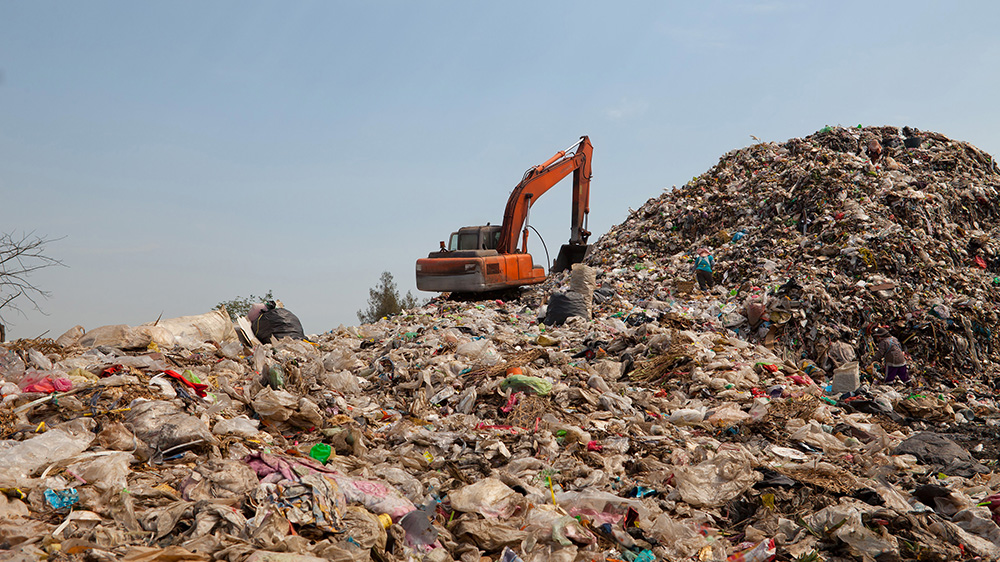 Backhoe moves trash in a landfill site, pollution