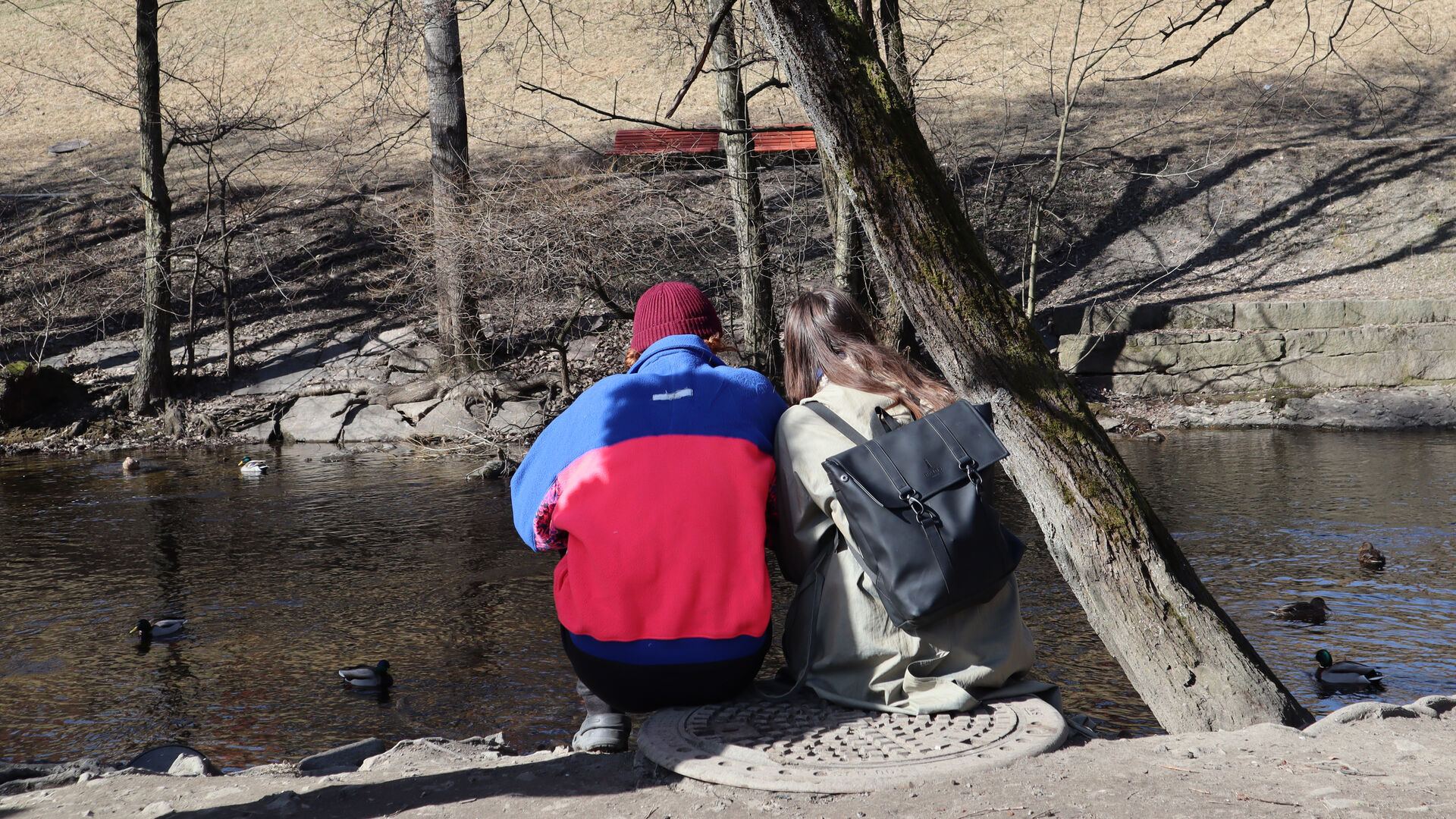 Students sitting by the Akerselva river side. Bare trees in the background