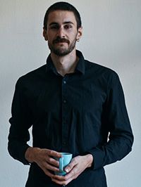 Portrait photo, man, dark hair, short hair, short beard, black shirt, holding a blue mug, indoors, white background
