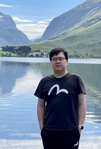 young man standing in front of a lake, valley and mountains in the background, black short hair, glasses on, black t-shirt and pants