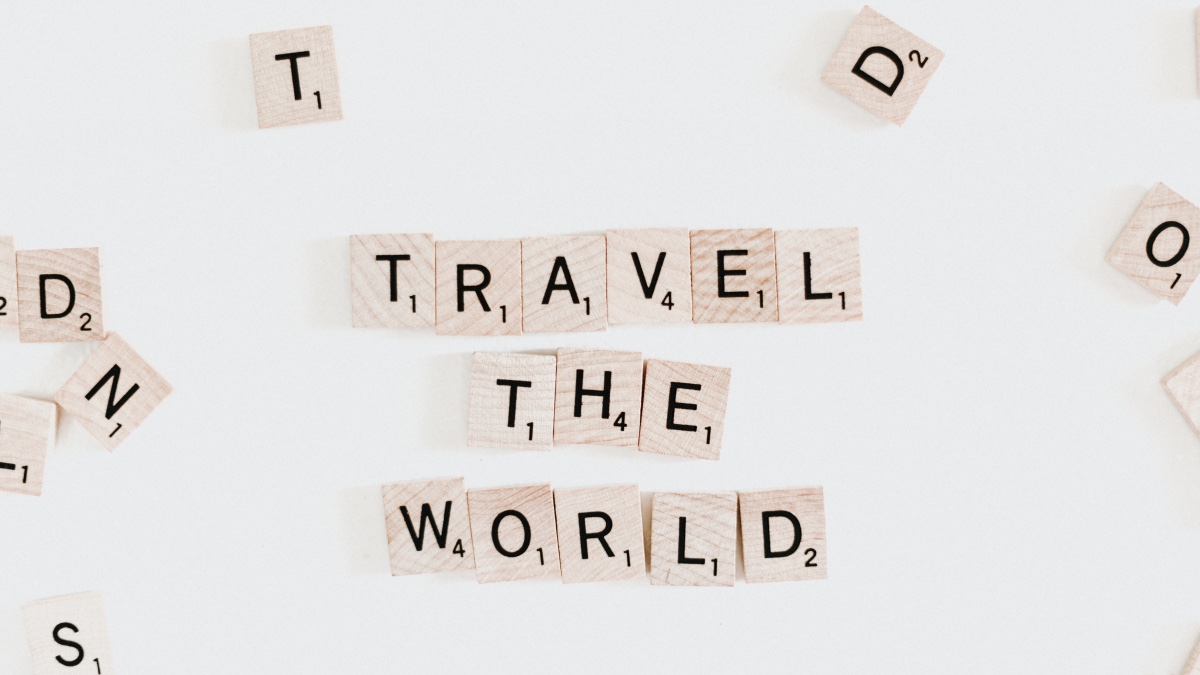 Scrabblebrikker på et bord som danner ordene "Travel the world". Foto.