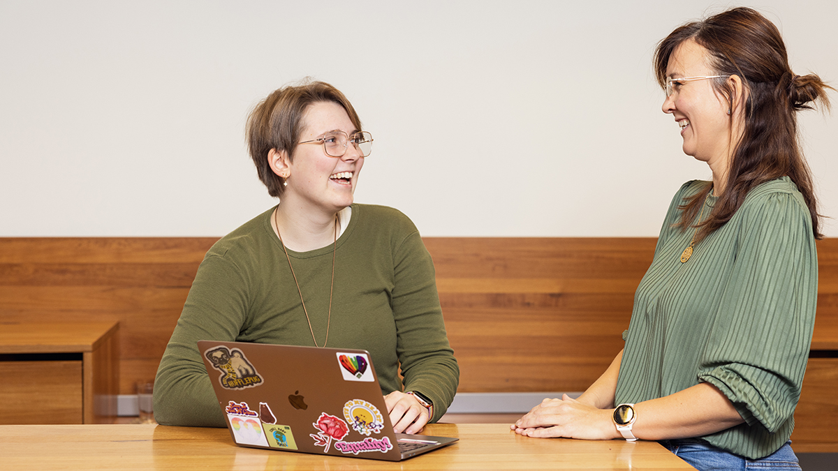Two women looking at a computer, talking and smiling. Photo.