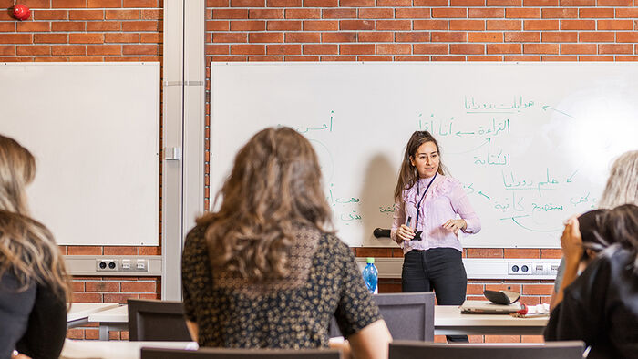 Et undervisningrom med studenter som sitter ved bordene og en underviser som står ved tavlen. Foto.