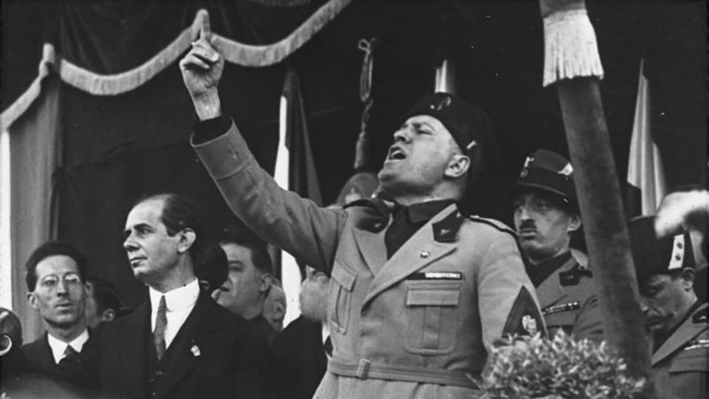 Svart hvitt bilde av Benito Mussolini - mann i uniform og uniformslue som hever pekefingeren.