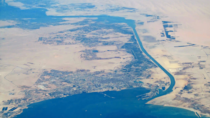 Aerial photograph of a desert landscape with the sea in the foreground. A canal runs through the landscape. Photo.