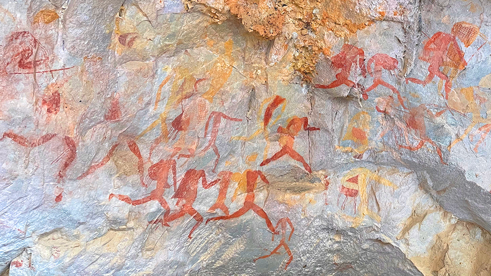 Mange røde menneskeskikkelser malt på en bergvegg. Fotografi. 