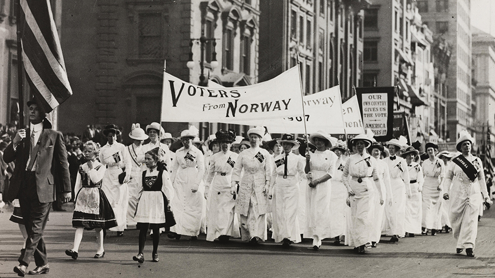 En gruppe med kvinner kledd i hvite drakter. De holder en parole der det st?r: "Voters from Norway". Svart-hvitt foto.  