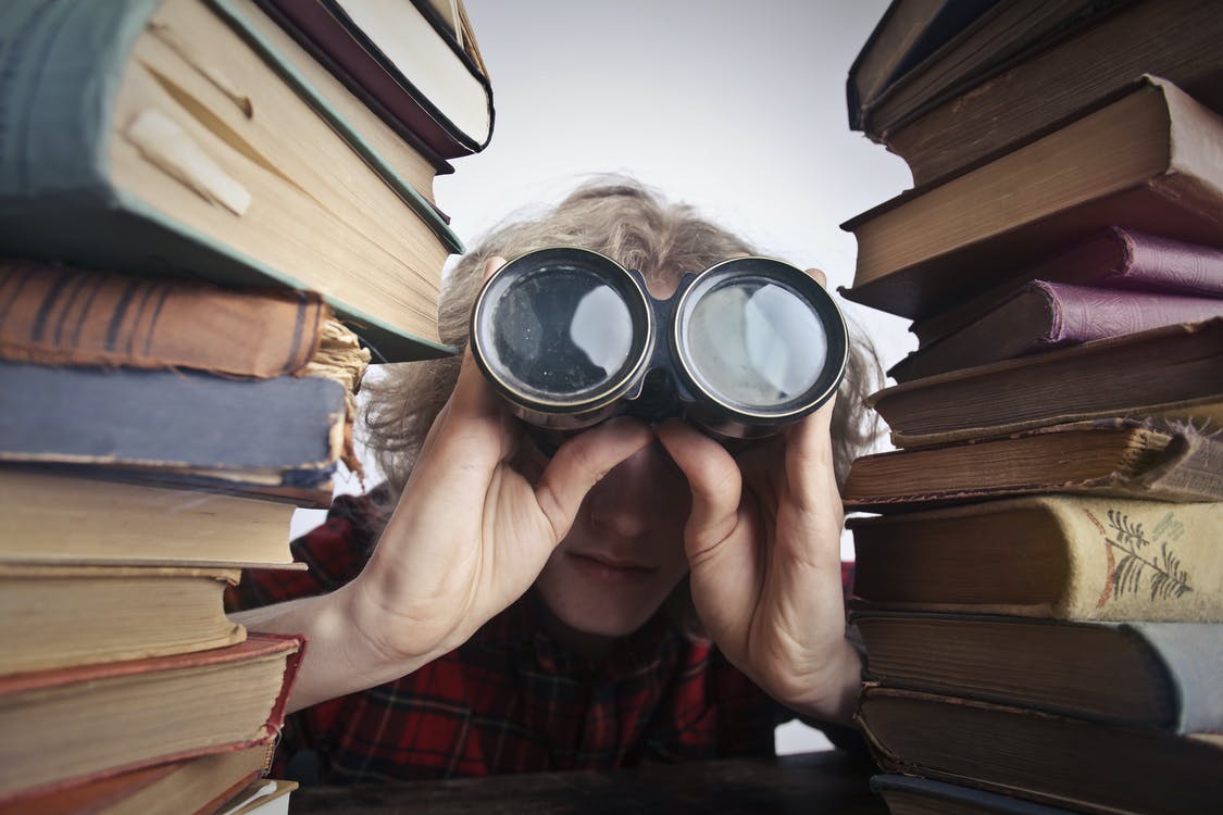 Bildet viser en person som ser på bøker med kikkert