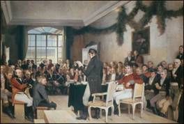  A man standing and talking in a nice room with other nice dresses men listening.