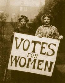 To kvinner holder opp en stor plakat der det står Votes for Women. Sort og hvitt.