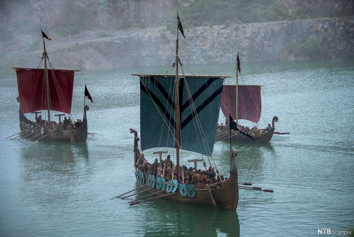 Maleri av tre vikingskip på åpen sjø. Havet og himmelen er i nyanser av blått og grått. 