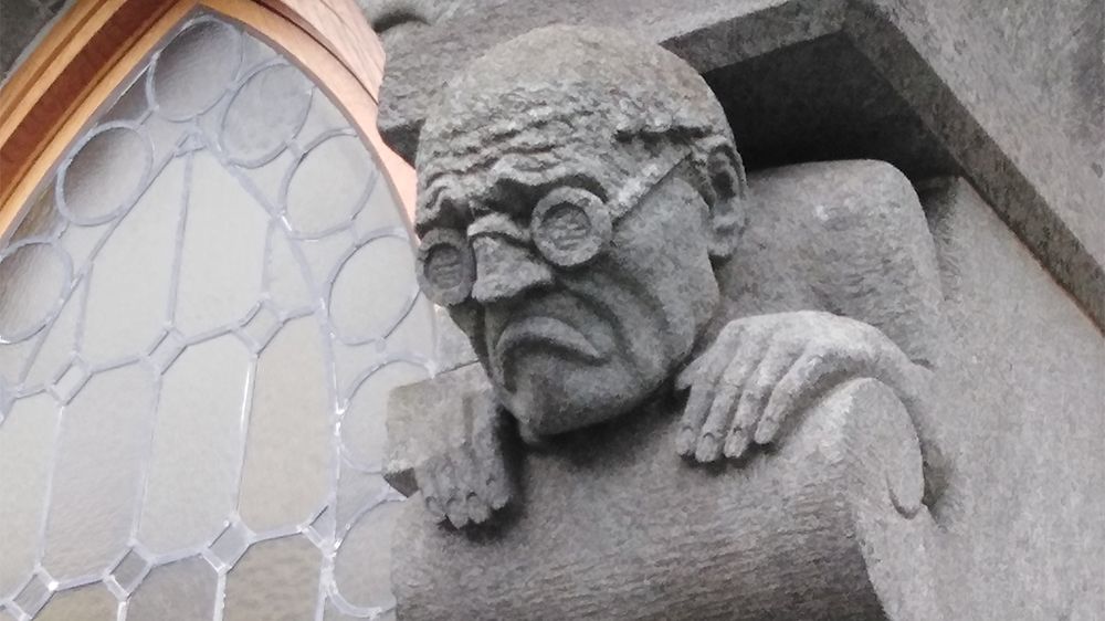 Steinornament av mann med briller og nedadgående munnviker.