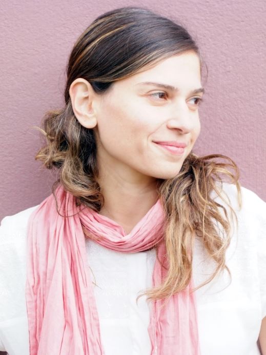 Woman, smiling, looking to the right, long hair, pink scarf, pink wall. 