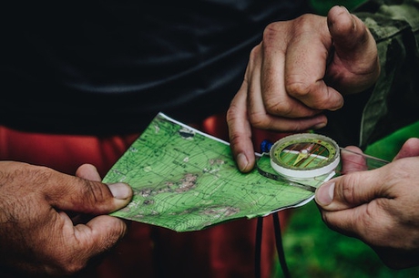 Hands holding map and compass. One hand pointing to a specific spot on the map