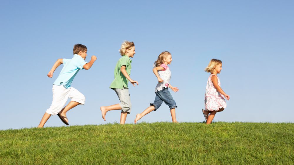 Four children running on grass on a sunny day. Photo.