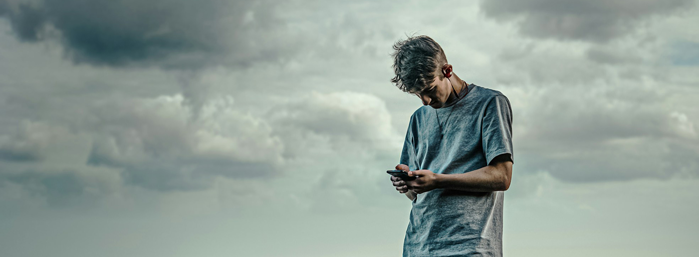 En ung mann ser på en mobiltelefon mens står på en stein ved sjøen.