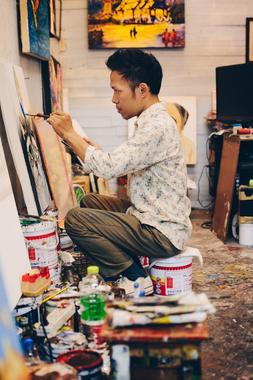 A man sitting on the ground painting a canvas