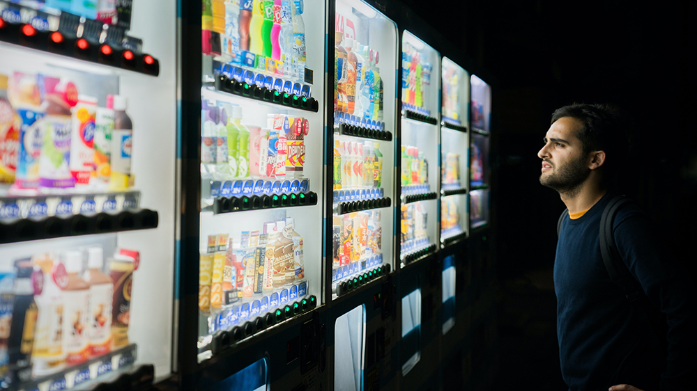 A man looking at an automat for soft drinks.