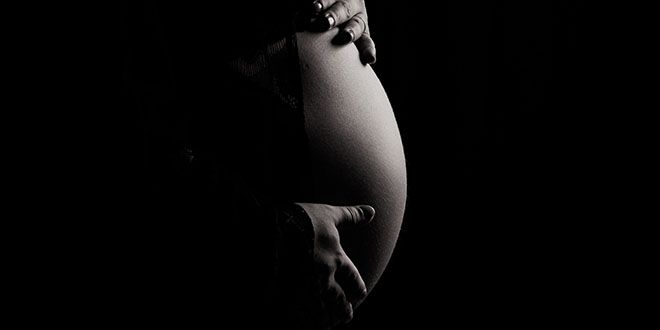 Pregnant belly with hands holding on it, photo in black and white.