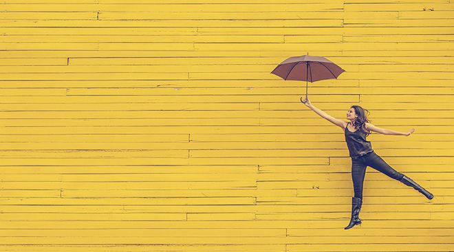 Woman with umbrella floating in front of a yellow wall 