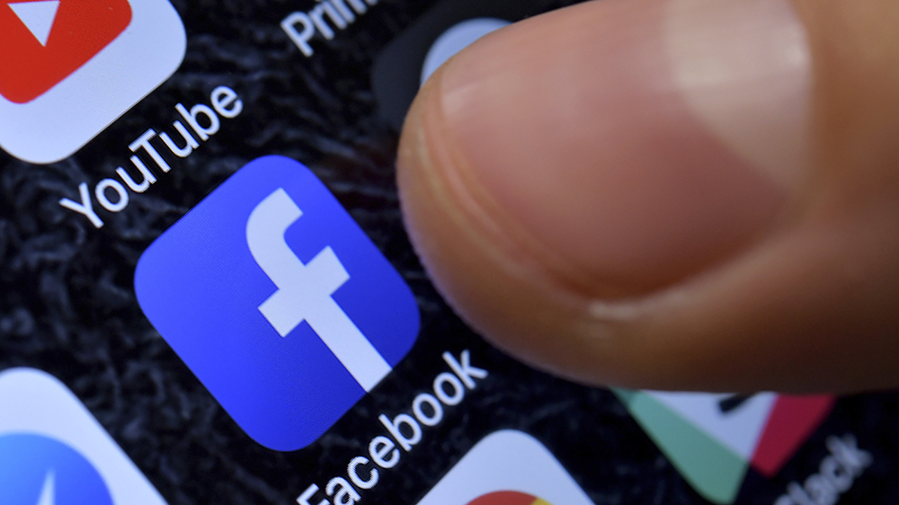 A finger directed towards the facebook app on a smart phone screen.
