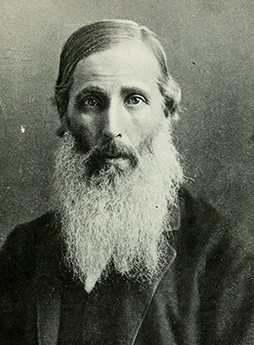 A black and white photo of an older man with a beard. He is looking straight ahead. Photo.