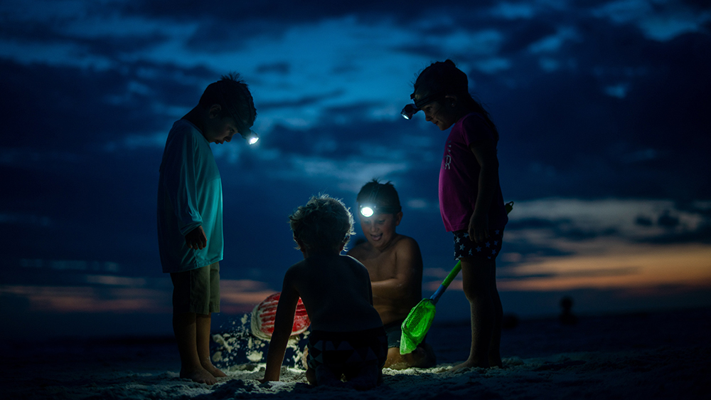 Fire barn med hodelykt på en strand om natten.