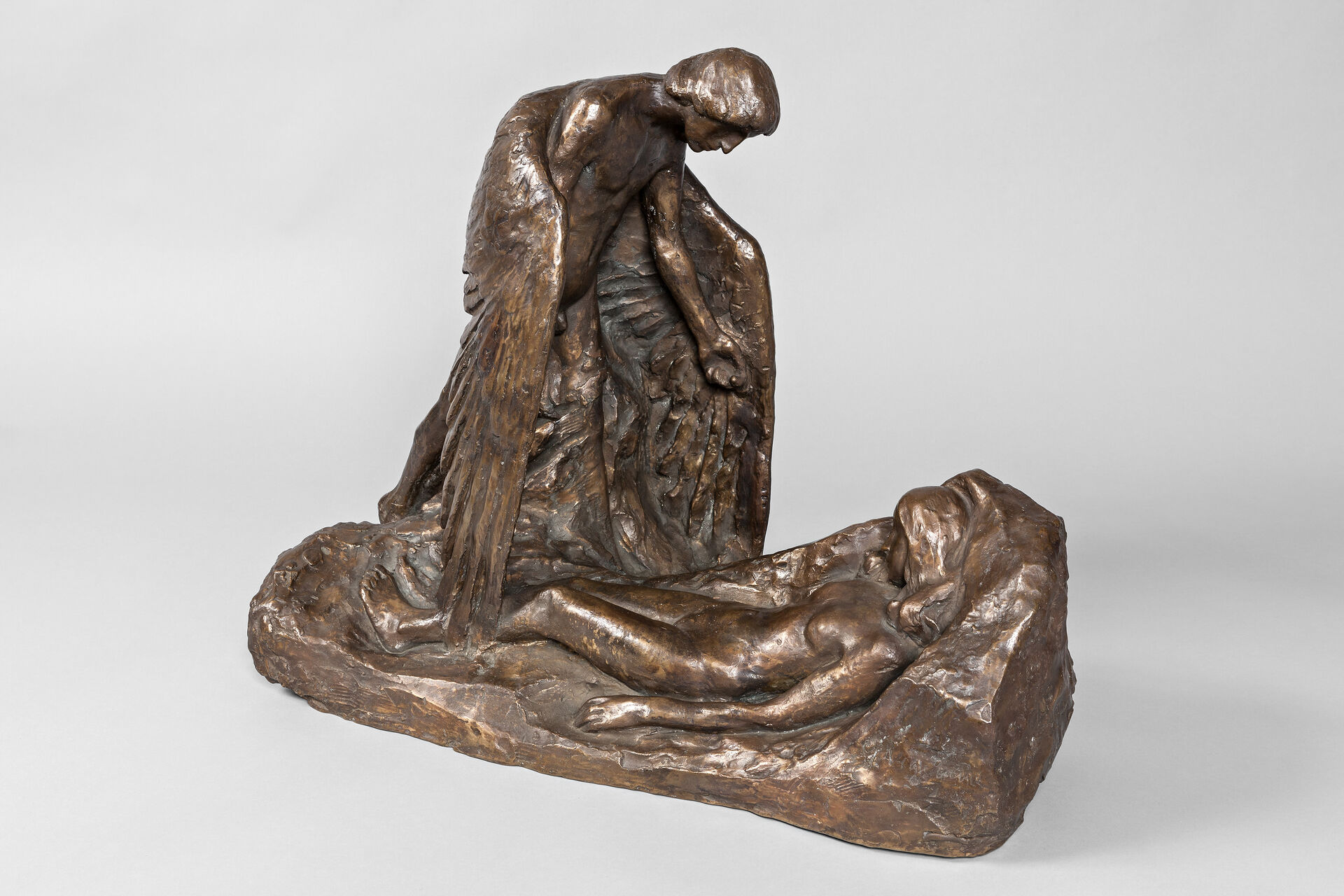 En person med vinger som står over en liggende kvinne. Skulptur i bronsje.