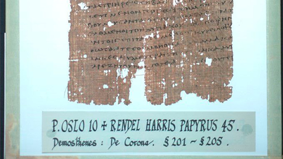 Tekst på slitt papyrus. Under er en etikken hvor det står: P. OSLO 10 + RENDEL HARRIS PAPYRUS 45. Demosthenes: De Corona. §201–§205.