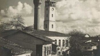 Black and white photo of two towers. Severeal buildings in the front. 