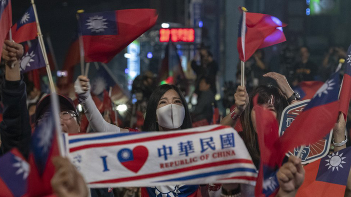 Image contains a woman with a white filter mask holding a banner that reads "I love the Republic of China" in Chinese characters. People around her carry Taiwanese flags.