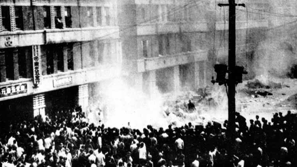 Image may contain a crowd of people standing by a column of smoke underneath a building facade.