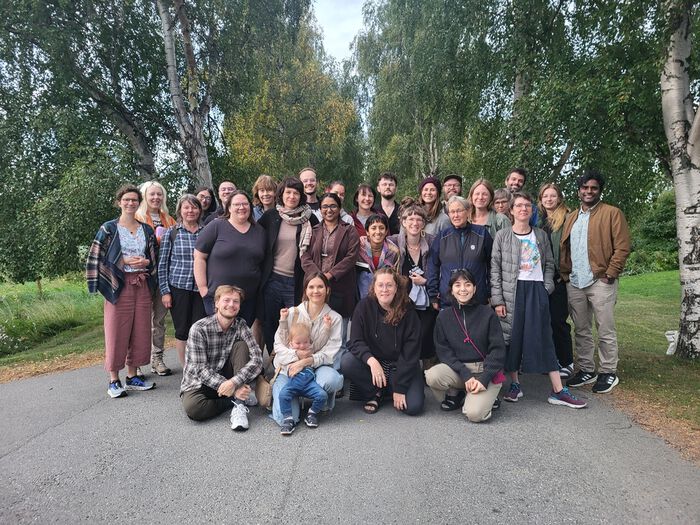 A group of people outdoors, surounded by green trees. Photo.