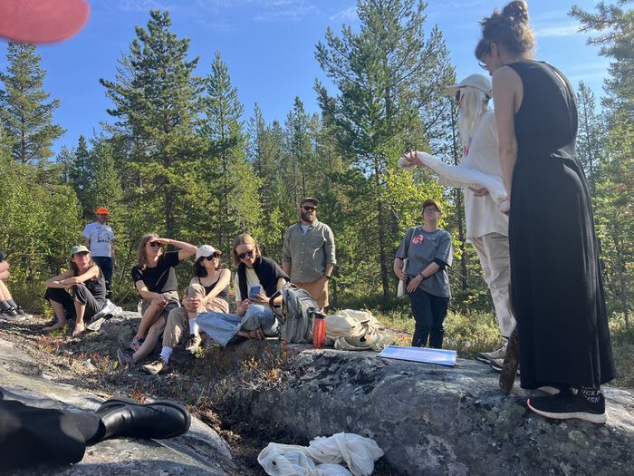 A group of people sitting together outside in the woods. Photo.