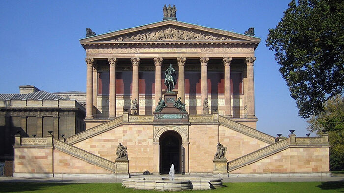 Green field in front. Big building with columns and steps in the back. 