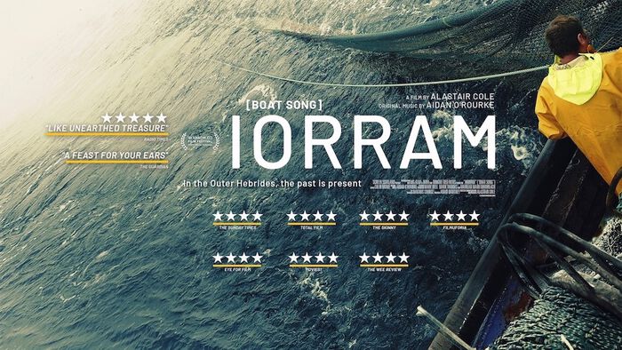 Promotional poster for the film Iorram (Boat Song), featuring a fisherman in yellow rain gear on a boat hauling in a net. 