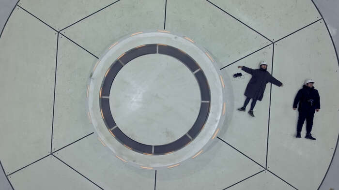 Overhead view of two people lying beside a large circular structure.