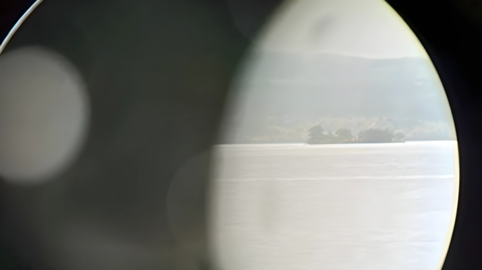 View of a body of water and distant shoreline through a circular lens, partially obscured by shadows.