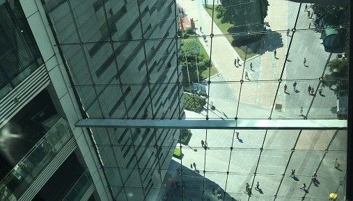 Ser ned fra høy bygning på glassvinduer som speiler mennesker  på bakkenivå.