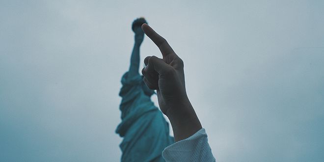 An index finger with the statue of liberty in the background.