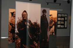 Exhibiton with photos of people, an old woman working outside in front.