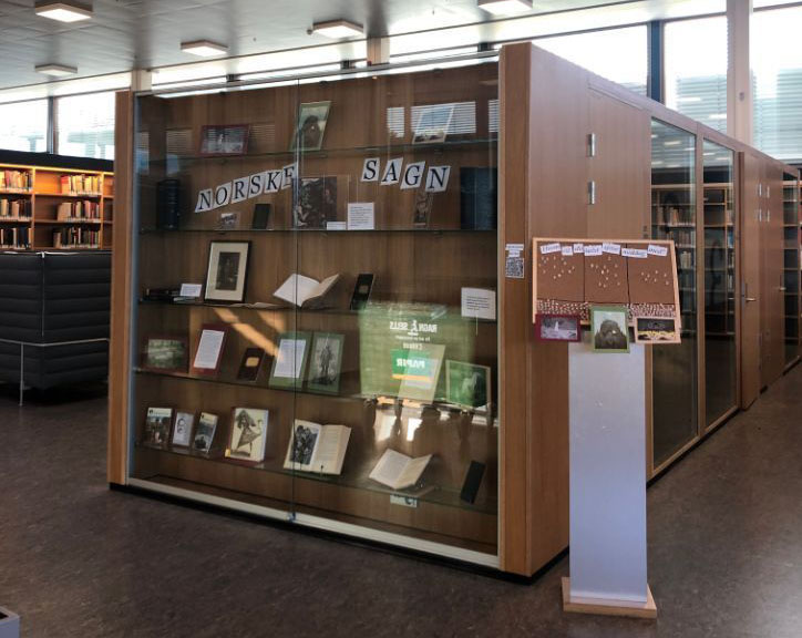 Utstillingsmonter med utstilte bøker, bilder og gjenstander fra norske sagn. Foto. 